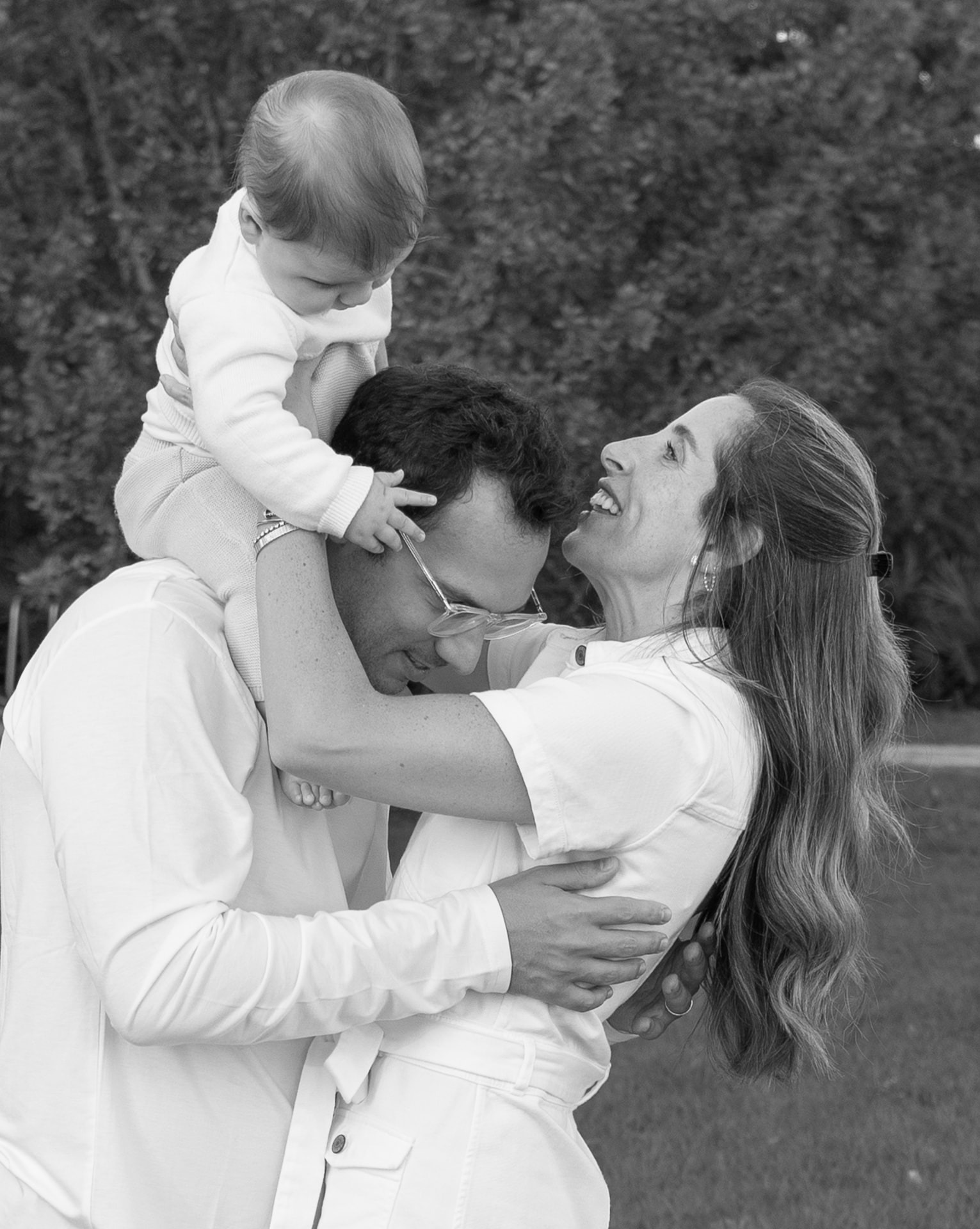 a mother laughing toward her baby held up beside her partner's head